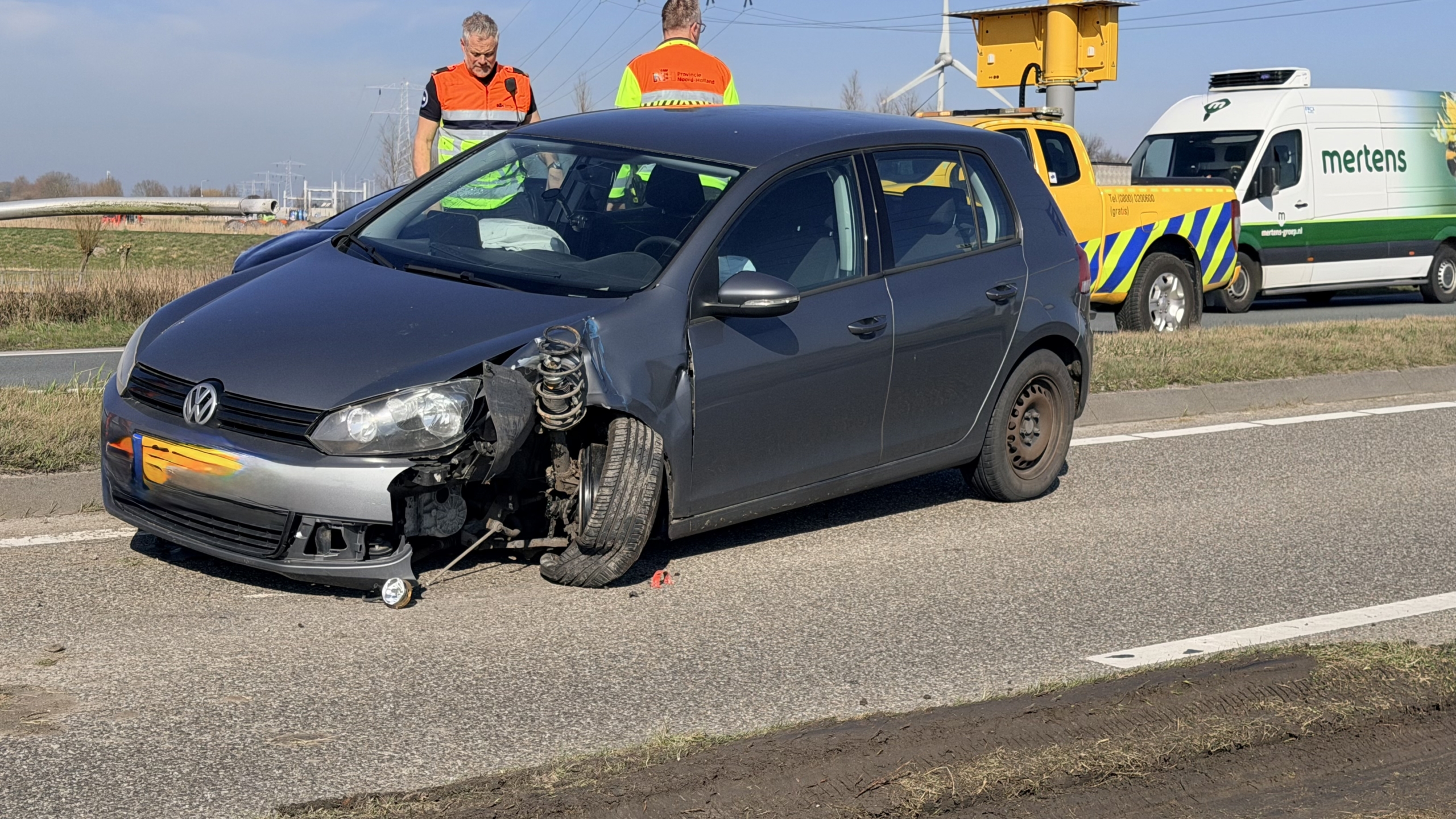 Verkeersongeval op een snelweg met een beschadigde auto en omgevallen lantaarnpaal, omringd door bergingsvoertuigen.