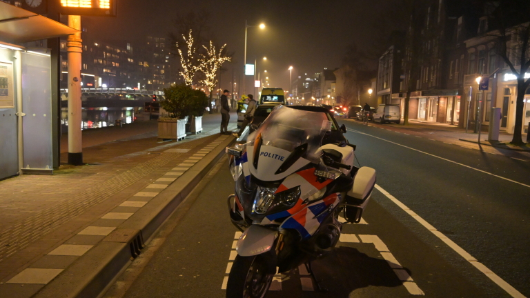 Ambulance en personenauto's langs de weg 's nachts met mensen erbij, in een verlichte stedelijke omgeving.