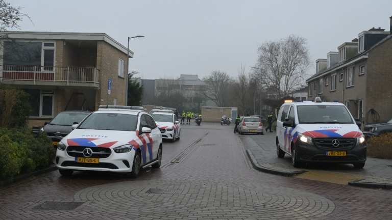 Politieagenten in uniform onderzoeken een plaats delict bij een flatgebouw, met een motor en een container in de buurt.
