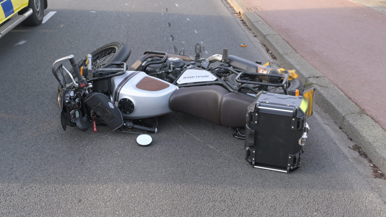Politieagenten en een ambulance bij een verkeersongeval met een omgevallen scooter op de weg, naast een geparkeerde auto.