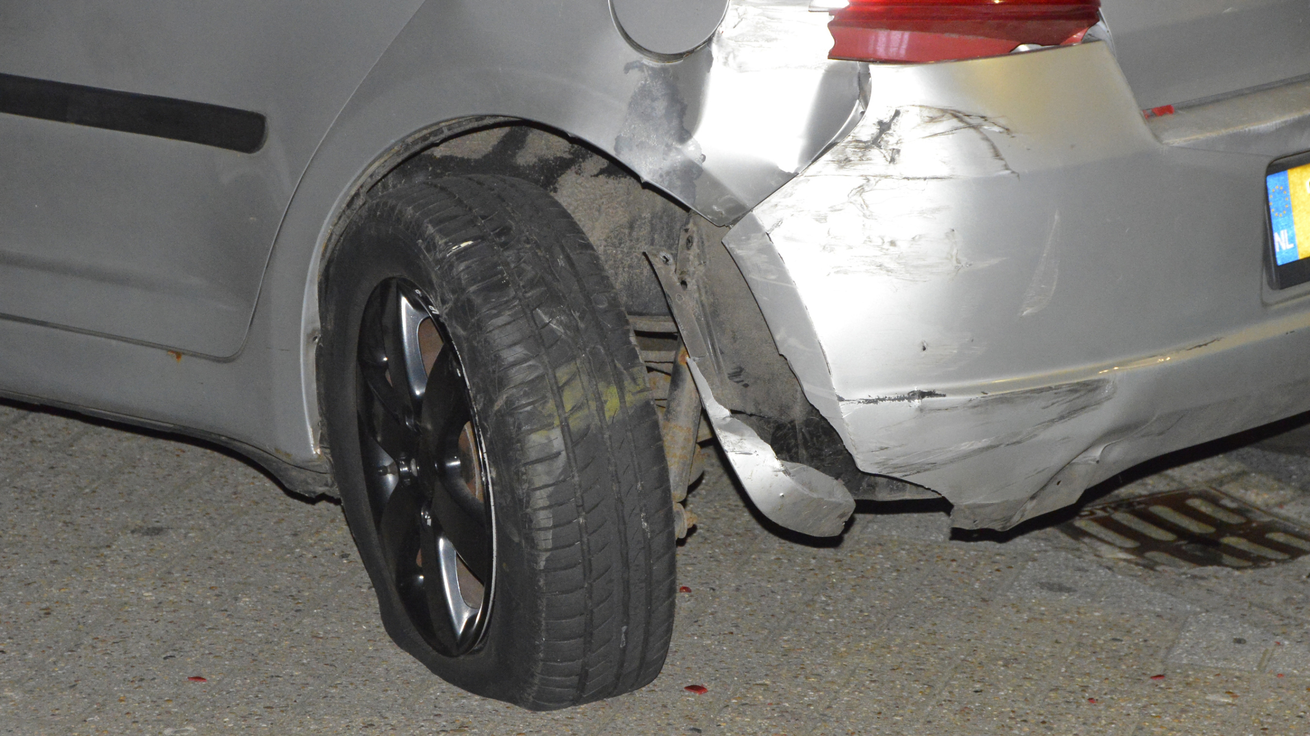 Twee auto's met schade op een parkeerplaats voor een MediaMarkt filiaal, omringd door mensen.