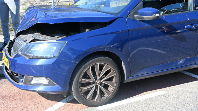 Twee auto's botsen op een weg met mensen die met een politieagent praten op de achtergrond.