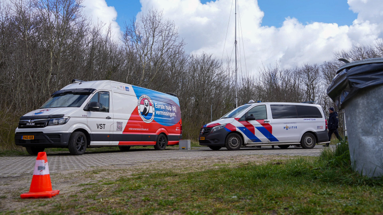Een groepje mensen in gele hesjes loopt met stokken door een bosrijk gebied met kale bomen.