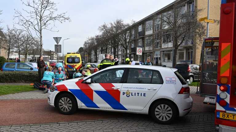 Hulpverleningsvoertuigen en mensen verzamelen zich bij een ongevalslocatie voor een gebouw.