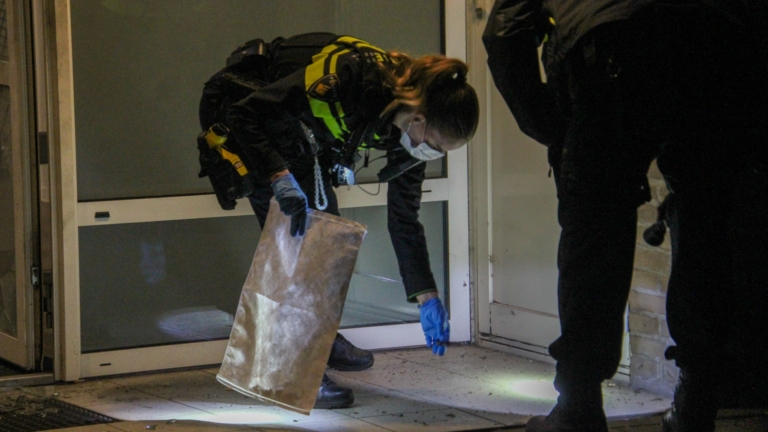 Bankje en gebroken glazen deur in een beschadigde hal met roet op het raam.