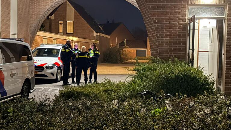 Politieagenten staan 's nachts bij politieauto's voor een gebouw met een open deur.