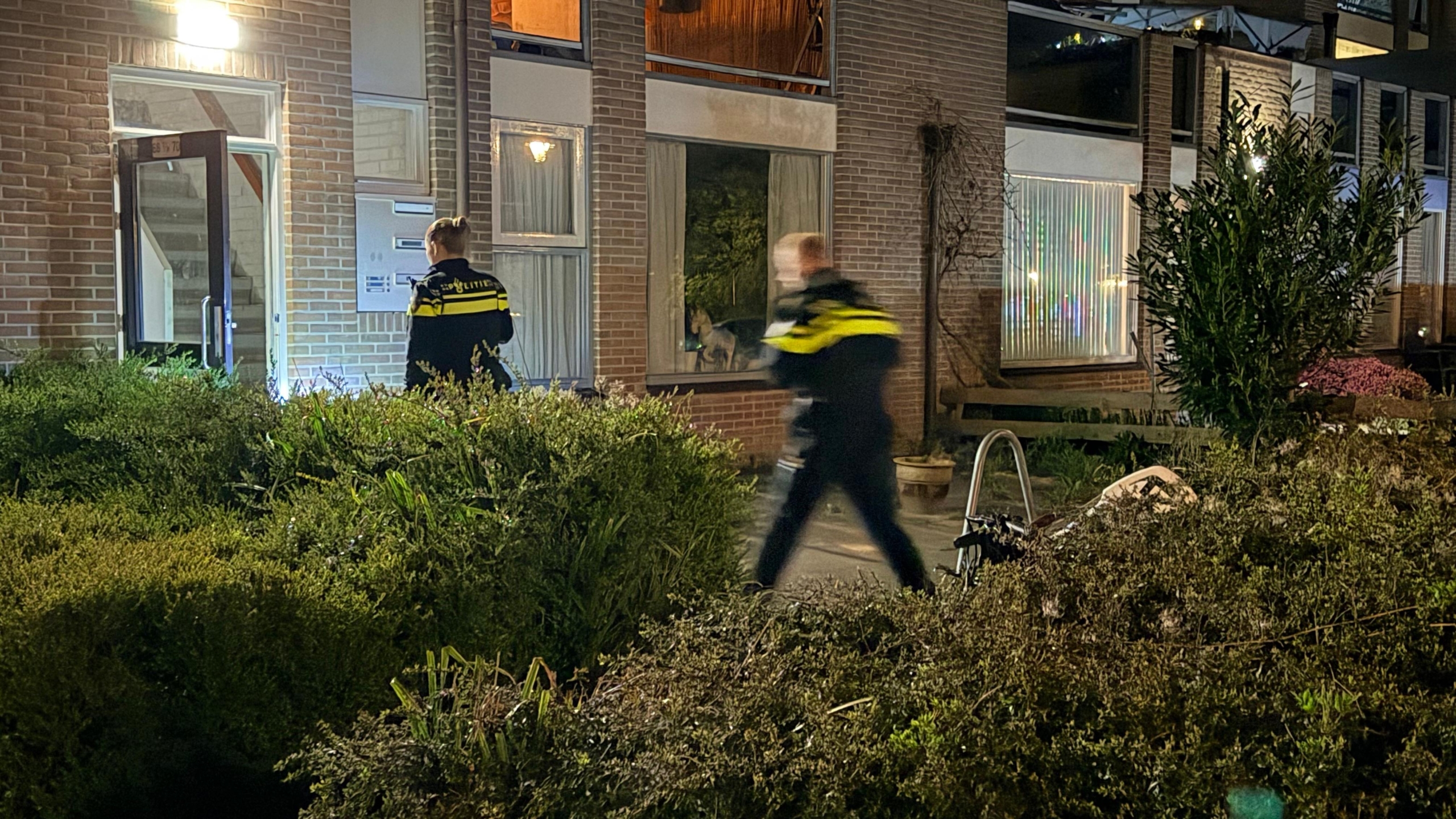 Politieagenten staan 's nachts bij politieauto's voor een gebouw met een open deur.