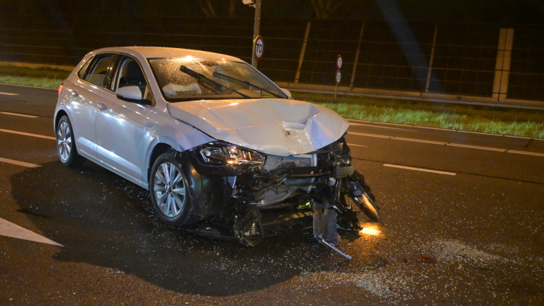 Verkeersongeluk in de nacht bij een kruispunt; ambulance en verschillende auto's aanwezig met politie en verkeerslichten op groen.