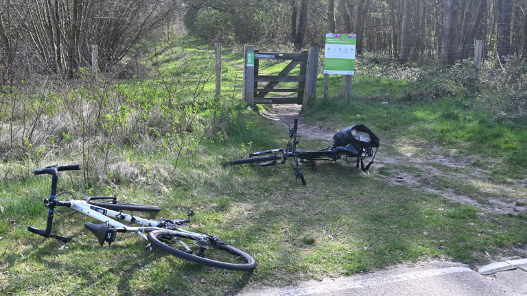 Ambulance met geopende deuren naast een weg, omringd door politieagenten en personen met fietsoutfits.