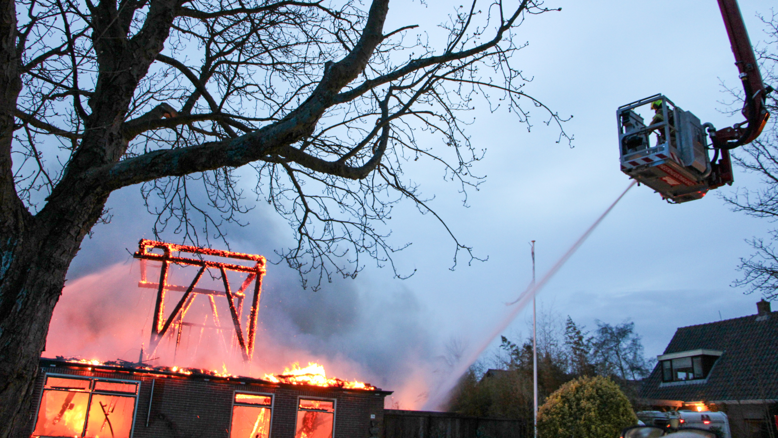 Brandweerlieden in volledige uitrusting bestrijden 's avonds een grote brand in een gebouw.