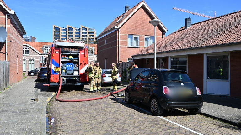 Brandweermannen naast een brandweerwagen in een woonwijk, met een brandslang aangesloten en huizen op de achtergrond.