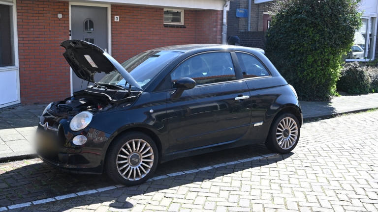 Brandweermannen naast een brandweerwagen in een woonwijk, met een brandslang aangesloten en huizen op de achtergrond.