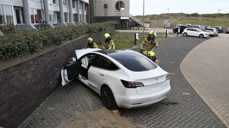 Brandweerlieden en politie bij een auto-ongeluk met een beschadigd voertuig; ambulance en politieagenten op de achtergrond.