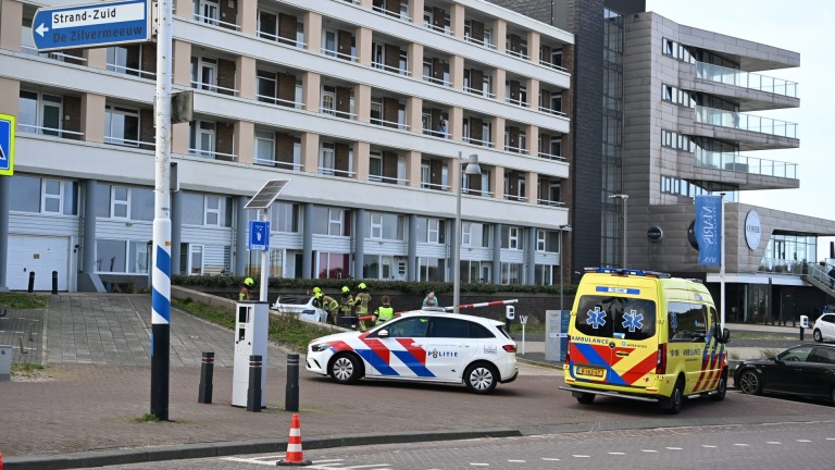 Brandweerlieden en politie bij een auto-ongeluk met een beschadigd voertuig; ambulance en politieagenten op de achtergrond.