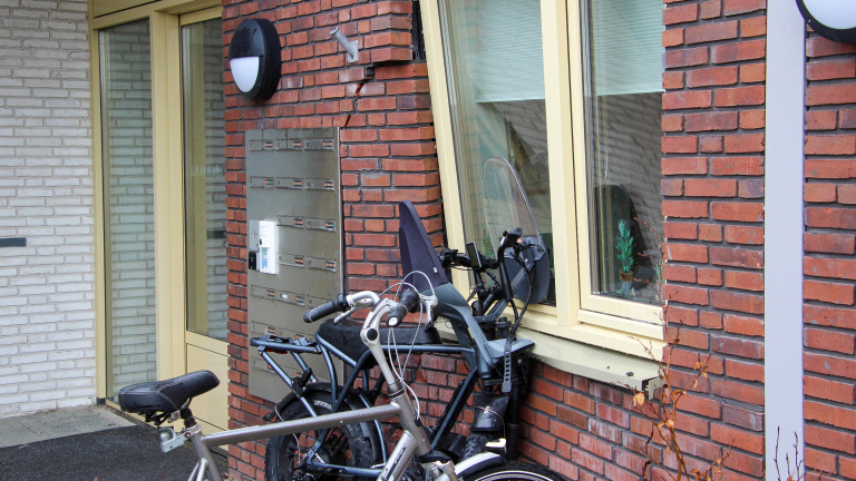 Fietsen geparkeerd naast een bakstenen muur met brievenbussen en een venster.