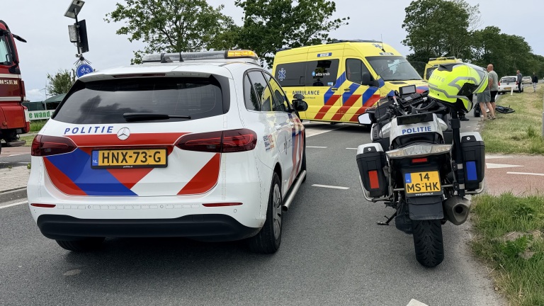 Politieauto, politiemotor en ambulance staan op straat bij een incident, met enkele mensen aan de rand van de weg.