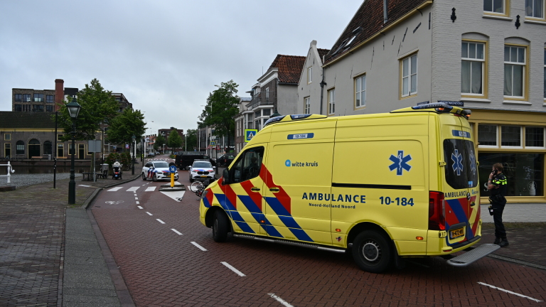 Omgevallen scooter en fiets op de weg naast politieauto's in een stedelijke omgeving.
