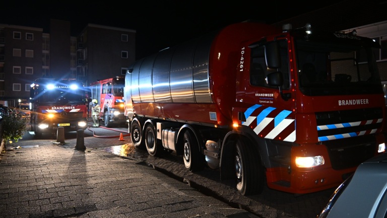 Brandweerwagens staan 's nachts geparkeerd voor een flatgebouw, met brandweerlieden aanwezig en heldere lichten aan.