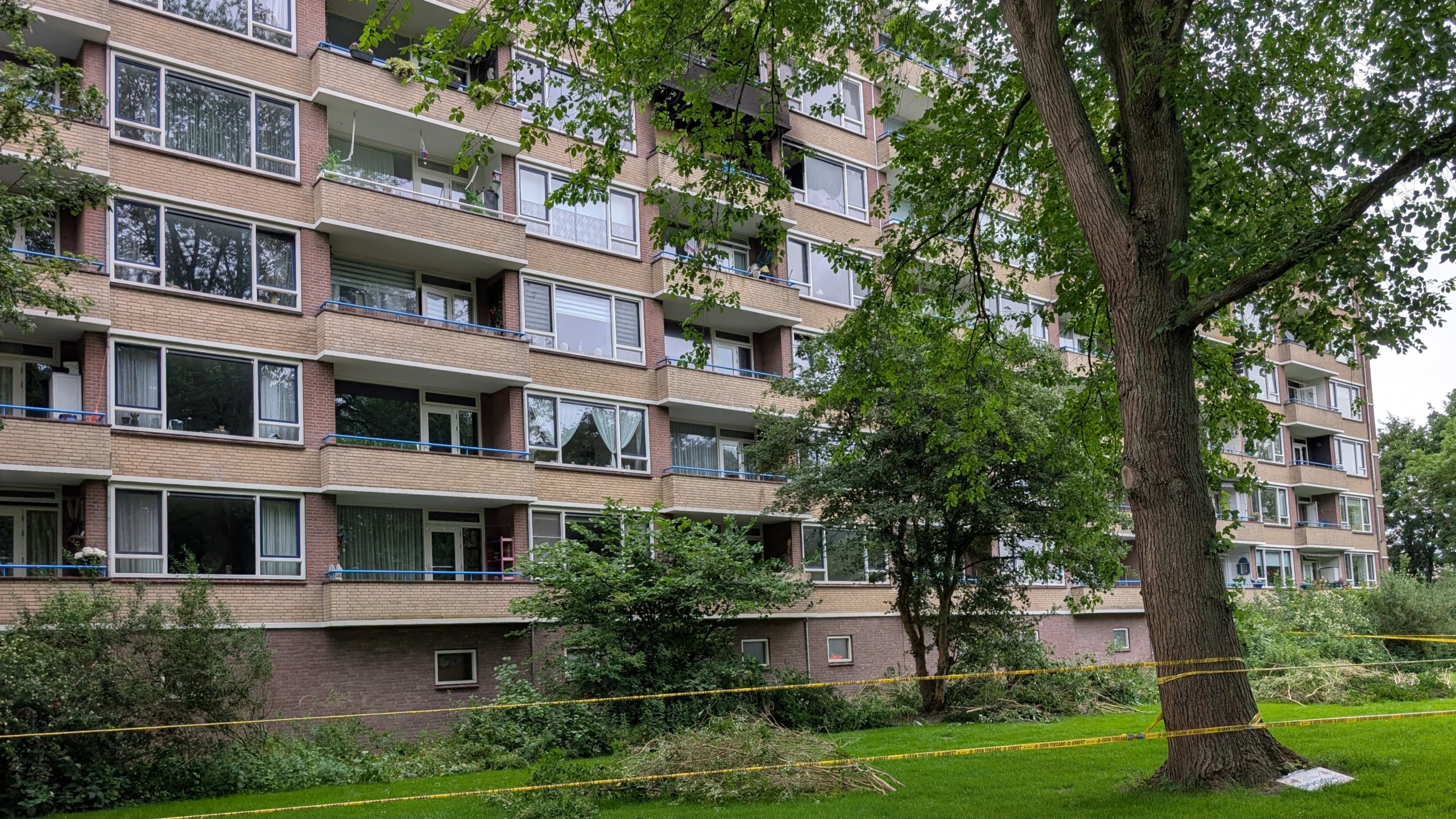 Wit bedrijfstrailer van Roessen & Roessen asbestsanering geparkeerd bij een appartementsgebouw, omgeven door waarschuwingslint.