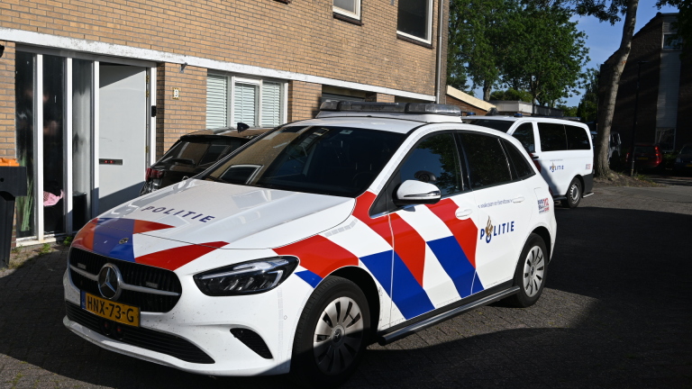 Een politieauto met rode en blauwe strepen staat geparkeerd voor een bakstenen gebouw.