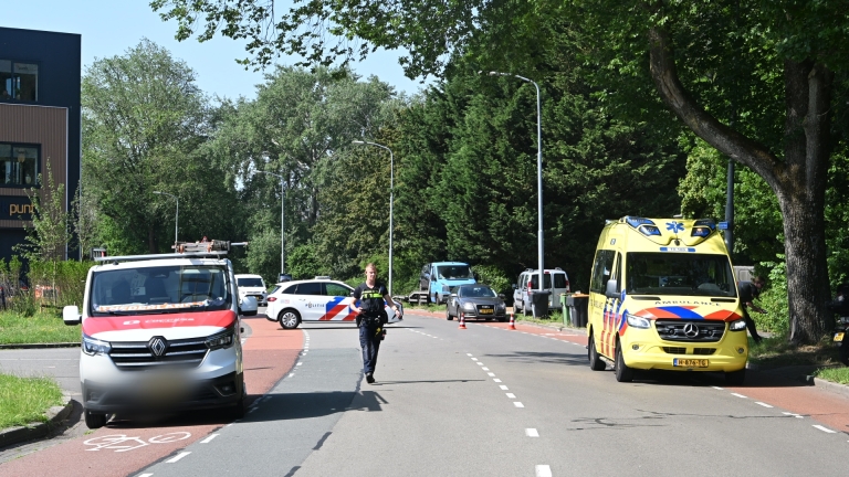 Een politiewagen naast een ambulance met een witte driewielige scooter en een helm op de stoep.