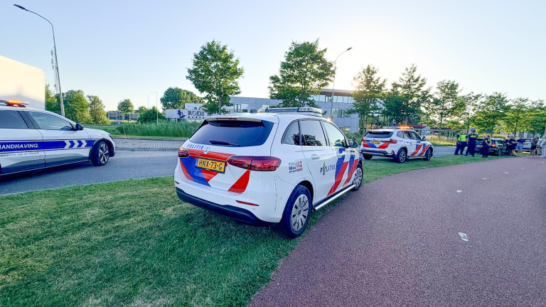 Politie- en handhavingsvoertuigen staan langs de weg, waar agenten met een groep mensen bezig zijn.