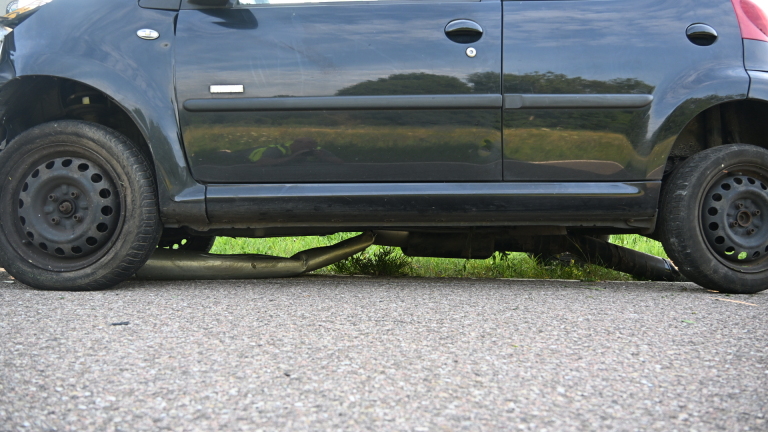 Auto gebotst tegen lantaarnpaal op rustige weg, met agent die schade inspecteert.