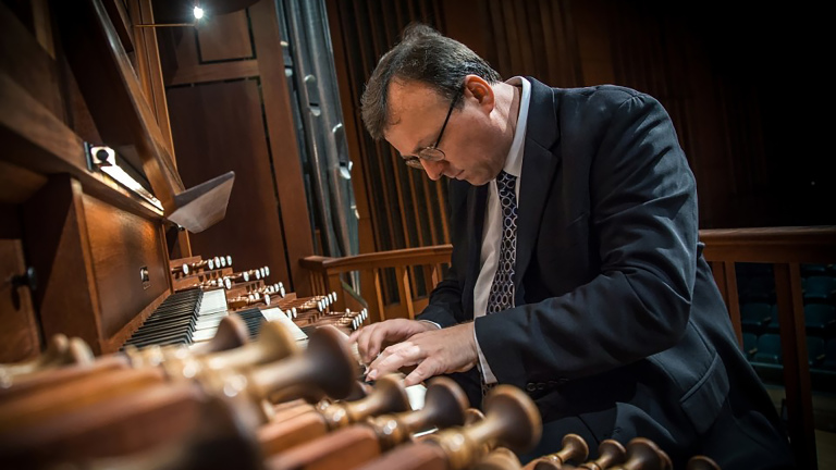 Twee musici: vrouw bij een orgel in een lichte ruimte en man in pak die geconcentreerd orgel speelt in een kerk