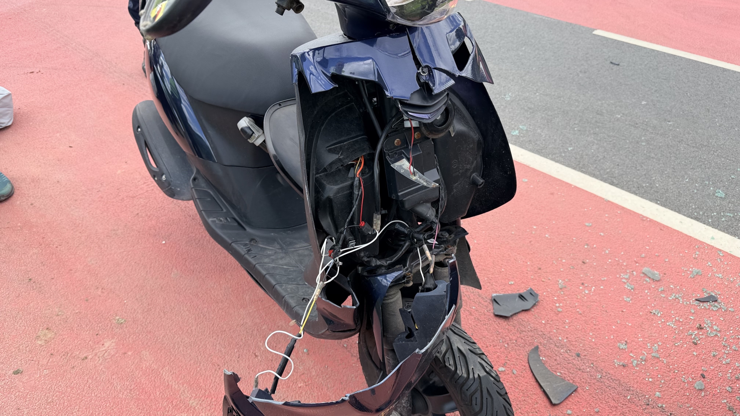 Achterkant van een BMW met ingeslagen achterruit en een beschadigde scooter op de voorgrond langs de weg