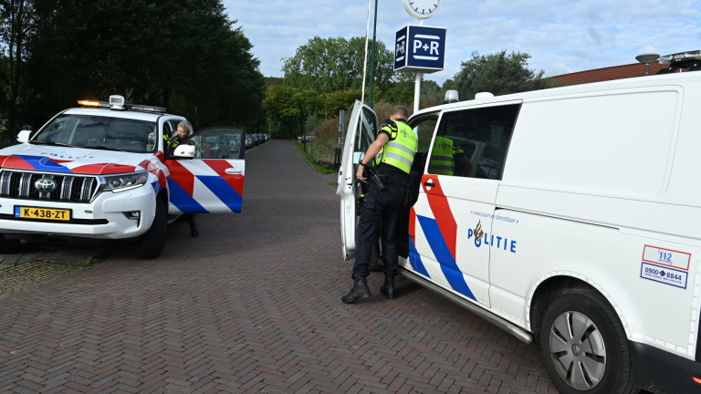 Politieagent en ambulancemedewerker bij blauwe auto met racefiets achterop in parkeervak, met omstanders ernaast
