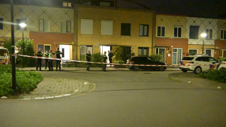 Twee politieagenten bij een politieauto ’s avonds op straat; één wijst omhoog, de ander houdt een diensthond vast