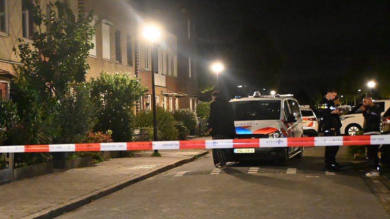 Twee politieagenten bij een politieauto ’s avonds op straat; één wijst omhoog, de ander houdt een diensthond vast
