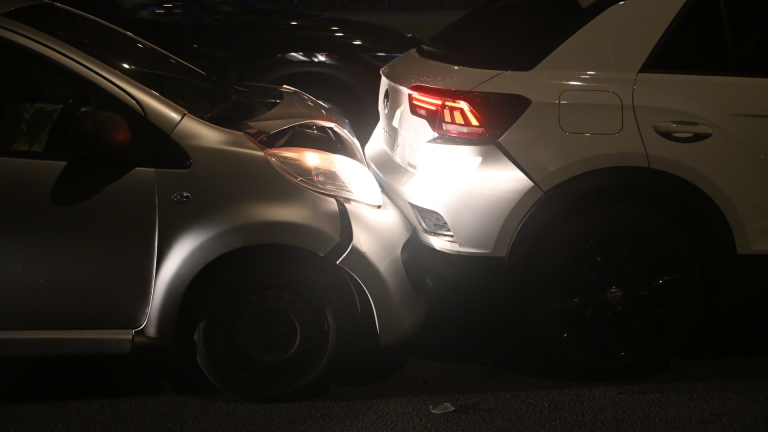 Kop-staartbotsing in het donker, met een grijze auto die achterop een witte auto is gereden