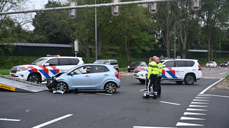 Beschadigde lichtblauwe auto wordt weggesleept na ongeval, met Nederlandse politieauto’s en agenten op kruispunt