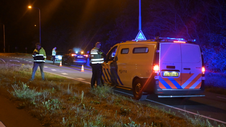 Politiecontrole ’s nachts met politiebusje met zwaailichten, agenten en kegels langs de weg