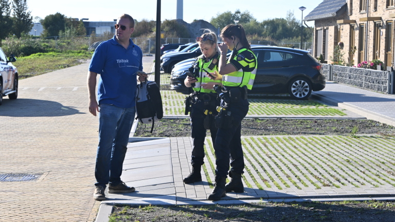Twee politieagenten in gele hesjes controleren gegevens op een telefoon terwijl een man met rugzak ernaast staat